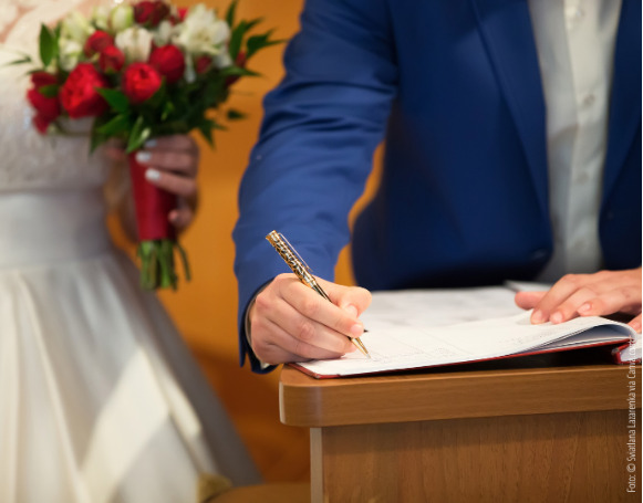 Brautpaar im Standesamt, der Bräutigam unterzeichnet die Hochzeitsurkunde